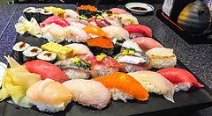 Piatto di sushi assortito su tavolo con persona in background.