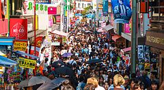 Una folla densa cammina lungo la via pedonale Takeshita Dori a Harajuku, circondata da insegne commerciali colorate.