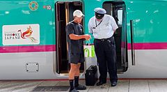 Persona interagisce con operatore ferroviario davanti a uno shinkansen alla stazione di Tokyo.