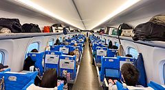 Interno di una carrozza passeggeri sul treno shinkansen con sedili blu occupati da persone e bagagli negli scomparti.
