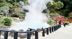 L'Umi Jigoku a Beppu con vapore denso che si alza dalla vasca azzurra accanto a un portale torii rosso.