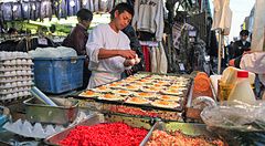 Venditore ad Ameyoko prepara cibo su griglia in un mercato vivace.