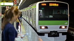 Un treno della linea Yamanote in arrivo in una stazione ferroviaria a Tokyo, in Giappone, con persone in banchina.