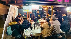 Persone sedute attorno a un bancone in uno yatai a Fukuoka, una tipica bancarella di cibo su strada illuminata la sera.