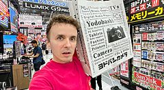 Marco Togni con busta di Yodobashi Camera in un negozio di elettronica.