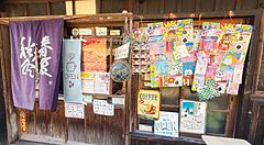 Facciata in legno dello Yoshijin Battari Cafe sull'isola di Nushima con un noren viola e insegne colorate.