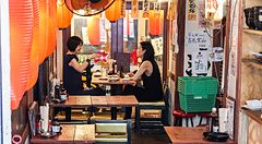 Interno di un izakaya a Yurakucho Yokocho, Tokyo, con persone sedute e lanterne rosse.