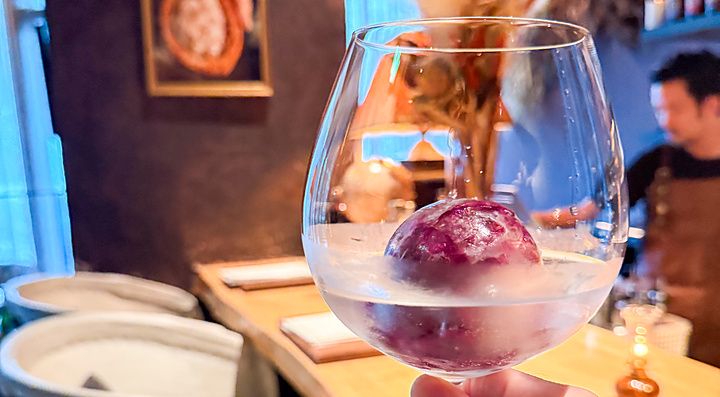 Un calice con cocktail e una sfera di ghiaccio tenuto in mano all'interno del bar Memento Mori a Tokyo.
