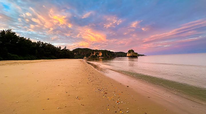 Una veduta della spiaggia Mimikiri Beach a Okinawa con sabbia dorata, vegetazione rigogliosa e un cielo al tramonto.