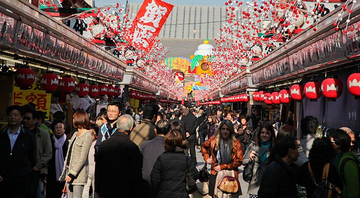 Folla di persone a Nakamise Dori, Asakusa, con decorazioni luminose e bancarelle.