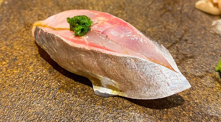 Un nigiri di aji con guarnizione verde servito su un piatto in ceramica scura da Sushi Takeuchi a Tokyo.