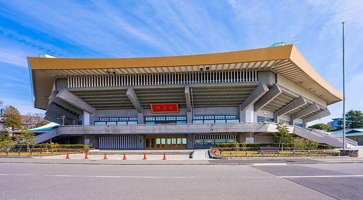 Facciata esterna del Nippon Budokan a Tokyo con tetto dorato sotto un cielo limpido e azzurro.