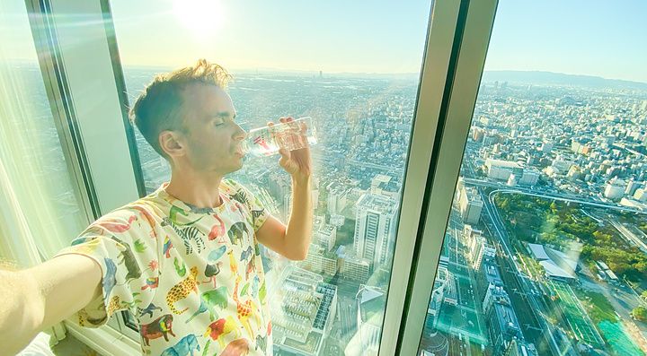 Una persona beve accanto a una finestra in una stanza d'hotel con vista sulla città.