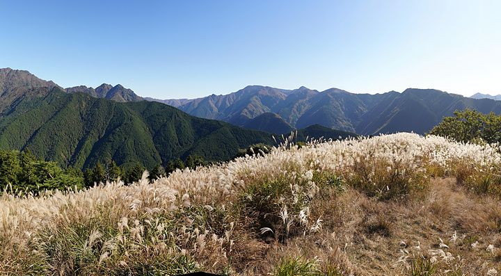 Veduta panoramica delle montagne di Omine Okugakemichi con campi di erba alta in primo piano sotto un cielo sereno.
