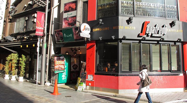 Una persona cammina sul marciapiede davanti a un locale Segafredo Zanetti all'angolo di una strada a Tokyo.