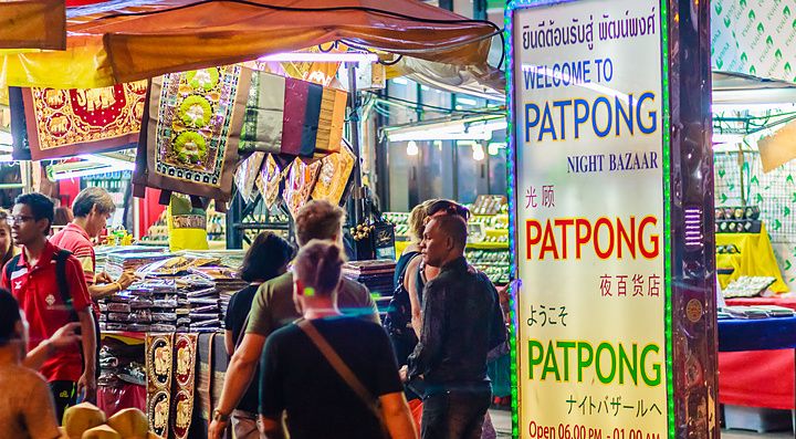 Scena notturna vivace al Patpong Night Bazaar di Bangkok con insegne luminose e bancarelle.