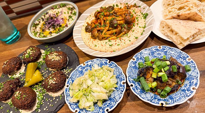 Piatti di falafel, hummus con funghi e pane pita serviti su un tavolo in legno nel ristorante Telaviv a Kyoto.