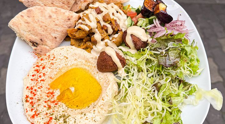 Un piatto misto vegano a Falafel Sababa composto da hummus, falafel, insalata e pane pita tenuto in mano a Namba, Osaka.