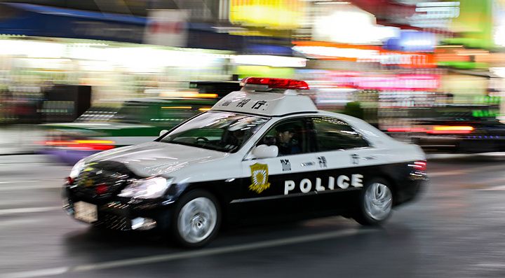 Volante della polizia giapponese in transito notturno lungo una strada urbana in Giappone.