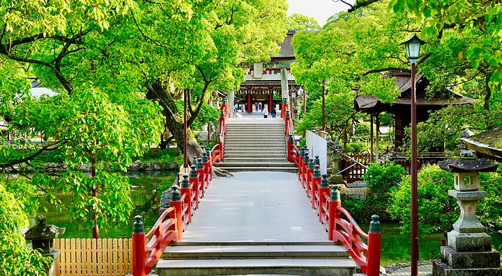 Ponte rosso ad arco che attraversa uno stagno in un parco alberato presso il santuario Dazaifu Tenmangu.