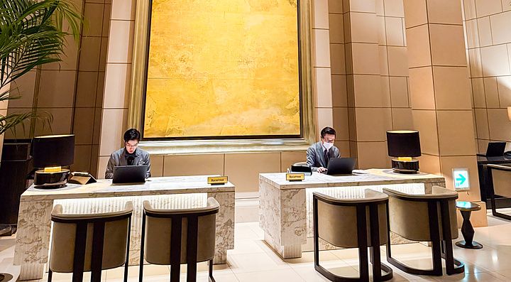 La reception a The St. Regis Osaka con due scrivanie in marmo, un grande dipinto dorato e un lampadario sferico.