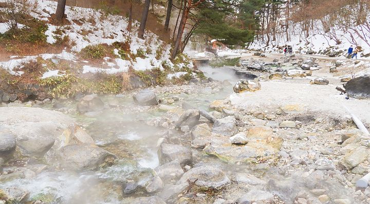 Veduta invernale di un ruscello termale nel Sainokawara Park, tra rocce, vapore e neve.