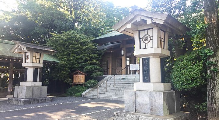 Due lanterne in pietra fiancheggiano il vialetto d'accesso verso una struttura in legno del Santuario Togo a Tokyo.
