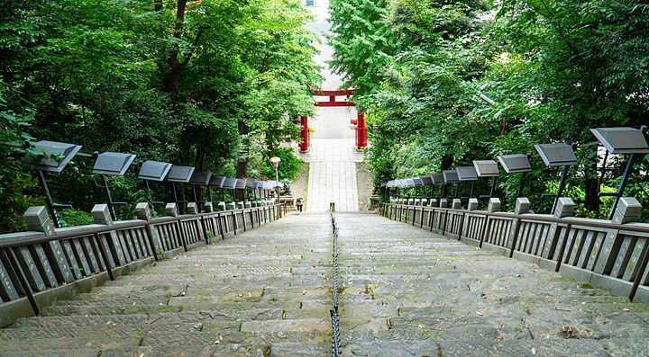 Ripida scalinata in pietra che scende verso un torii rosso circondato da alberi verdi al santuario di Atago a Tokyo.