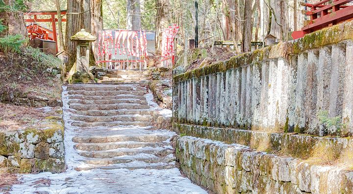 Santuario shintoista di Takinoo a Nikko con una scalinata in pietra innevata e un muro di cinta in pietra antica.