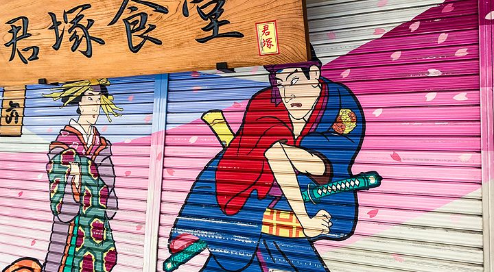 Una saracinesca di un negozio ad Asakusa decorata con un murales di un samurai accanto a un'insegna in legno.