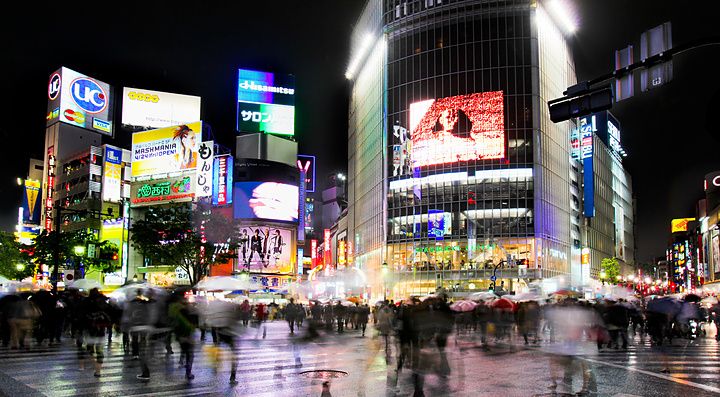 Incrocio di Shibuya a Tokyo con pioggia e persone sotto ombrelli.