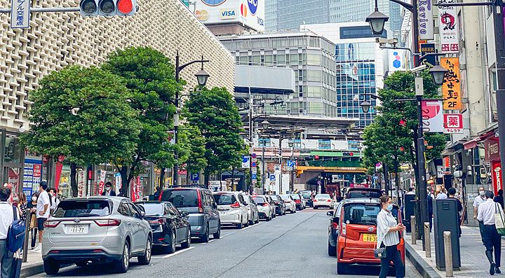 Una strada urbana a Shimbashi con il New Shinbashi Building sulla sinistra e vari edifici commerciali.