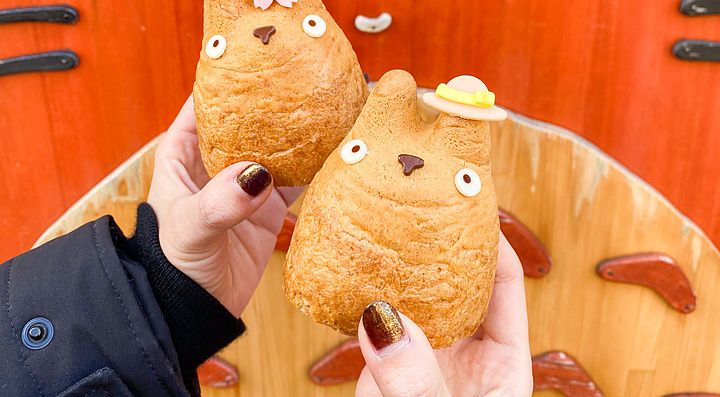 Due bignè a forma di Totoro tenuti in mano davanti a una decorazione in legno del personaggio presso la Shirohige’s Cream ...