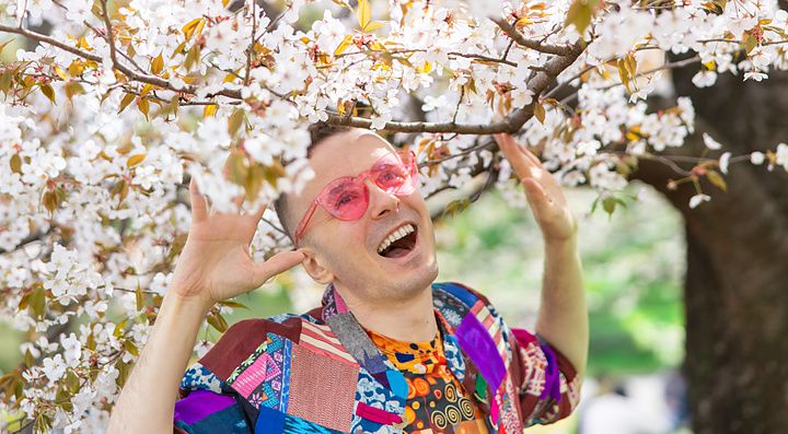 Marco Togni sorridente sotto un albero di ciliegio in fiore a Tokyo.