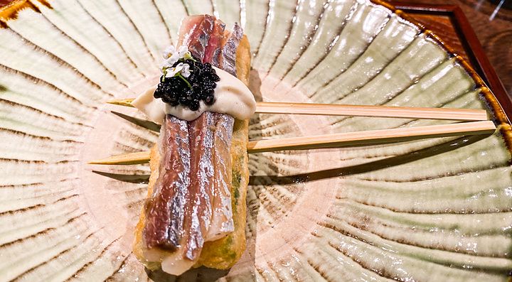Uno spiedino con yuba fritta e sugarello crudo, con crema e caviale servito su un piatto in ceramica al Denkushiflori.