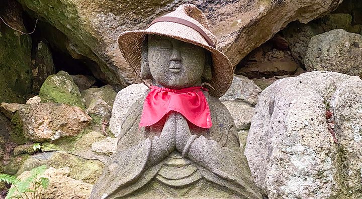Una statua in pietra di una divinità buddista con cappello di paglia e bavaglino rosso al Tempio di Risshakuji.