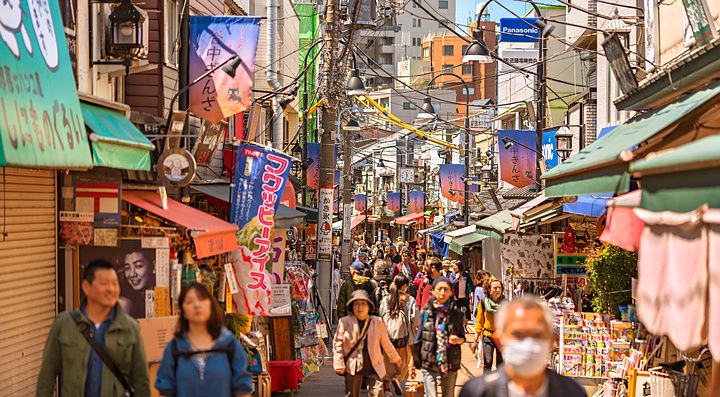 Persone camminano lungo la stretta via commerciale Yanaka Ginza a Tokyo, circondata da negozi tradizionali e insegne.