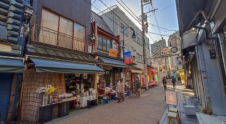 Veduta di una tipica strada storica del quartiere Yanaka a Tokyo con negozi e persone che camminano.