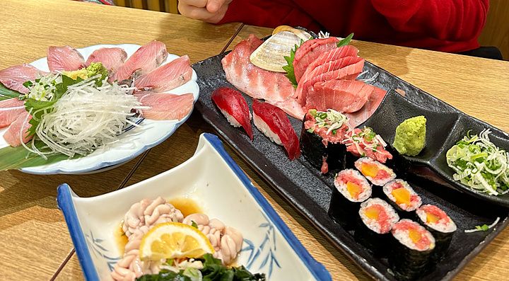 Marco Togni sorridente fa il gesto di vittoria davanti a piatti di sushi e sashimi nel ristorante Sushi no Darihan a Shinj...