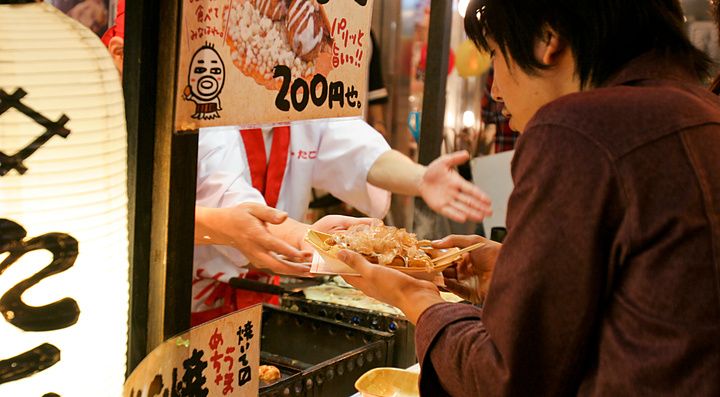 Un venditore consegna takoyaki ad un cliente presso un chiosco ad Osaka.