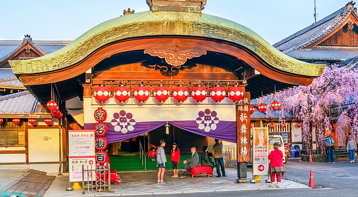Ingresso del teatro Gion Kobu Kaburenjo a Kyoto, con lanterne rosse, tende viola e ciliegi in fiore.