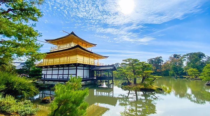 Il Tempio d'Oro, Kinkaku-ji, si specchia nelle acque di uno stagno circondato da alberi sotto un cielo azzurro luminoso.