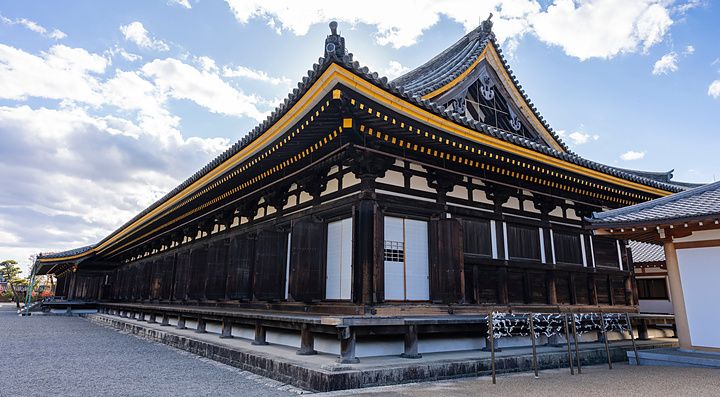 Edificio del tempio Sanjusangendo a Kyoto con facciata in legno scuro e finiture dorate sotto un cielo azzurro.