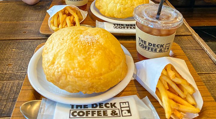 Marco Togni con occhiali rosa siede a un tavolo con hot pie, patatine e bibite al caffè presso The Deck Coffee & Pie.