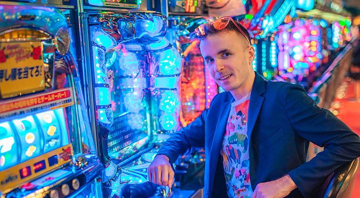Marco Togni seduto davanti a una macchina da pachinko illuminata in una sala giochi.
