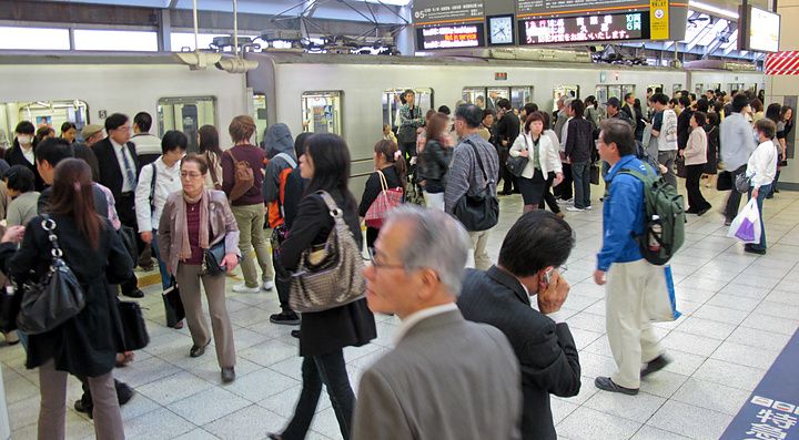 Persone in attesa sulla banchina affollata di una stazione ferroviaria a Tokyo, in Giappone.