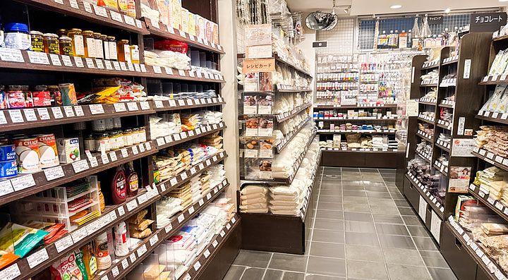 Interno del negozio Tomizawa Shoten a Machida, con scaffali in legno pieni di prodotti alimentari e da pasticceria.