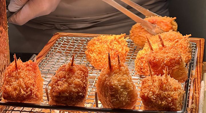 Chef che utilizza delle pinze per maneggiare pezzi di tonkatsu fritto su una griglia al Ginza Katsukami di Tokyo.