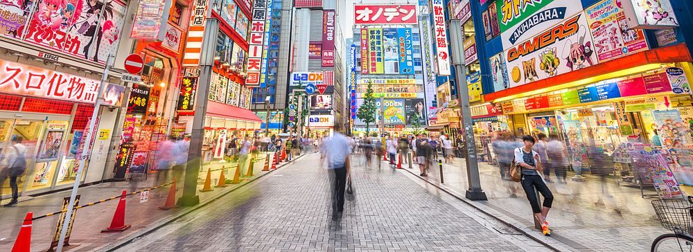 Street di Akihabara a Tokyo, con insegne colorate e folla in movimento.
