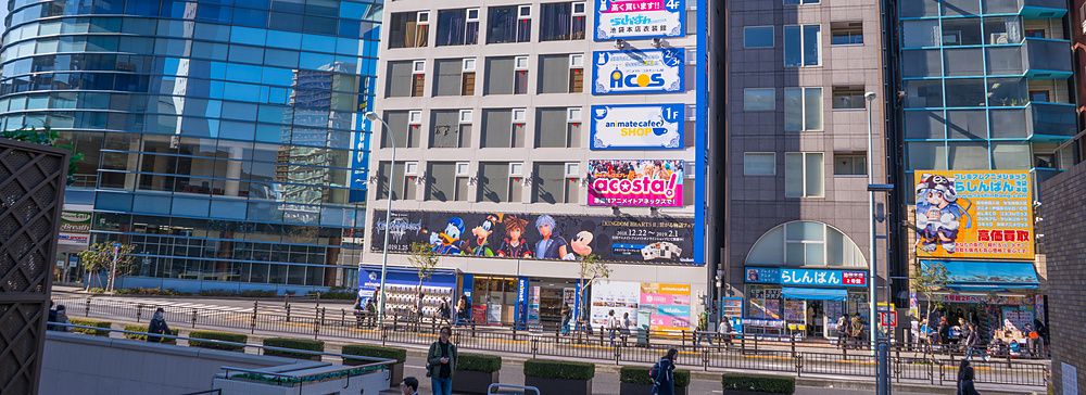 Edificio Animate Annex a Ikebukuro con insegne colorate e passanti che camminano sul marciapiede in un giorno di sole.